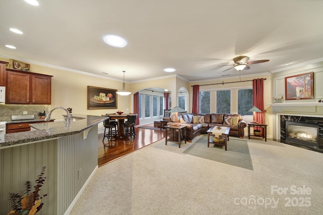 living room featuring crown molding, ceiling fan, a premium fireplace, and sink