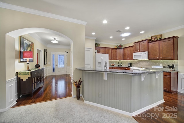 kitchen featuring crown molding, a breakfast bar, dark stone countertops, and white appliances