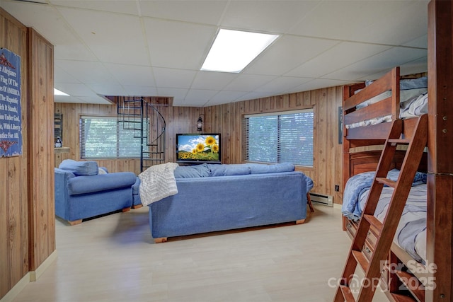 living room with a drop ceiling, wood walls, a baseboard heating unit, and light hardwood / wood-style floors