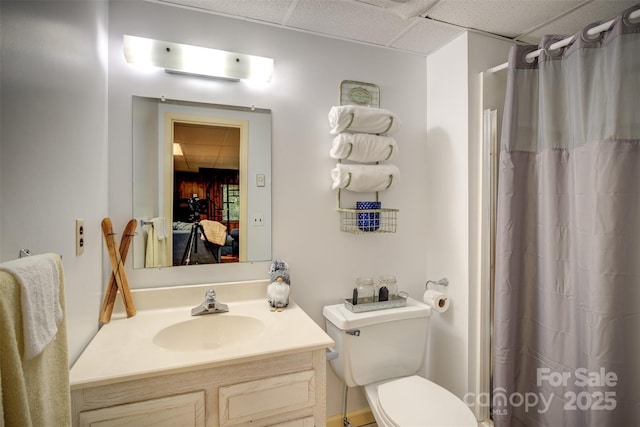 bathroom with toilet, a shower with shower curtain, a drop ceiling, and vanity