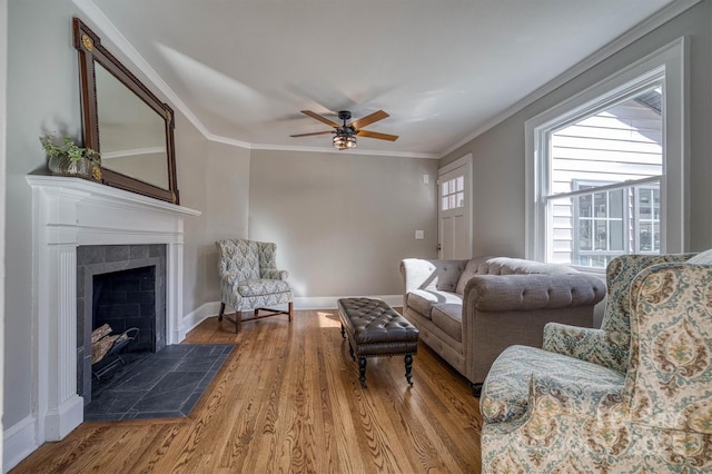 living room featuring a tiled fireplace, hardwood / wood-style floors, crown molding, and ceiling fan