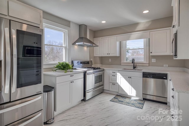 kitchen featuring wall chimney range hood, sink, white cabinets, and appliances with stainless steel finishes