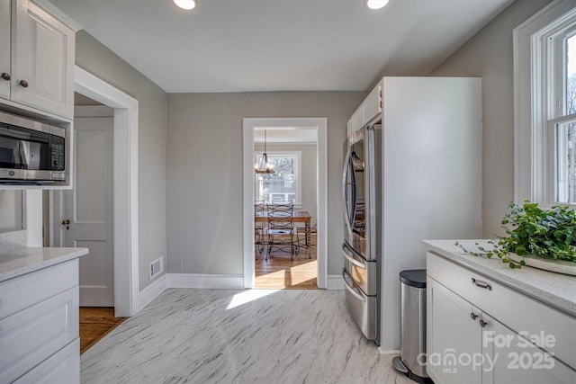 kitchen with pendant lighting, appliances with stainless steel finishes, an inviting chandelier, light stone counters, and white cabinets