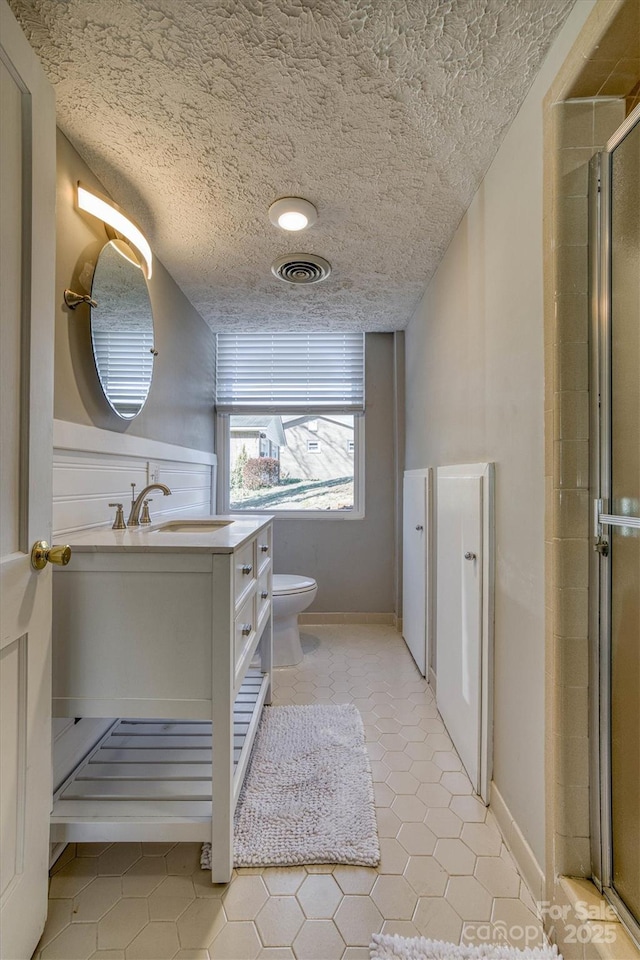 bathroom featuring vanity, toilet, a textured ceiling, and a shower with shower door