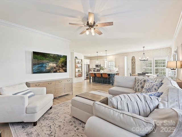 living room featuring light wood-type flooring, ceiling fan with notable chandelier, brick wall, and a healthy amount of sunlight