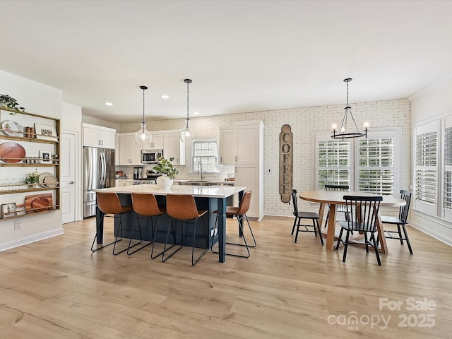 kitchen with a center island, appliances with stainless steel finishes, hanging light fixtures, white cabinets, and light hardwood / wood-style flooring