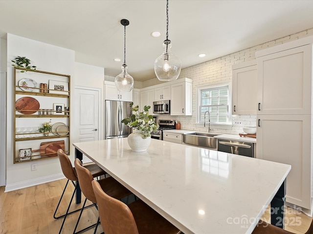 kitchen with pendant lighting, sink, white cabinetry, a kitchen island, and stainless steel appliances