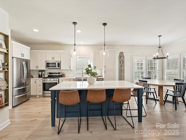 kitchen featuring pendant lighting, white cabinets, appliances with stainless steel finishes, a kitchen island, and sink