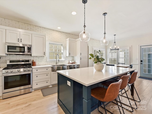 kitchen featuring a center island, appliances with stainless steel finishes, white cabinetry, sink, and decorative light fixtures