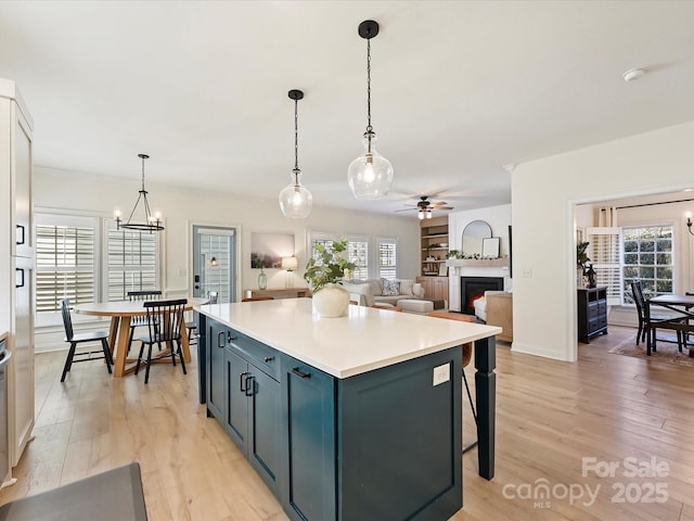 kitchen featuring ceiling fan with notable chandelier, a kitchen island, decorative light fixtures, a kitchen breakfast bar, and light hardwood / wood-style flooring