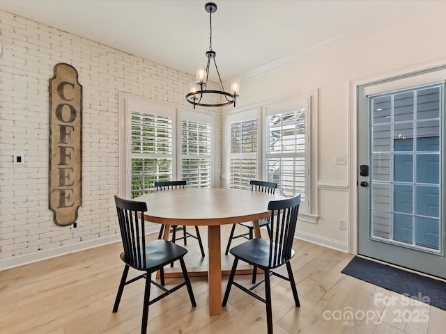 dining space with light hardwood / wood-style floors, brick wall, and an inviting chandelier