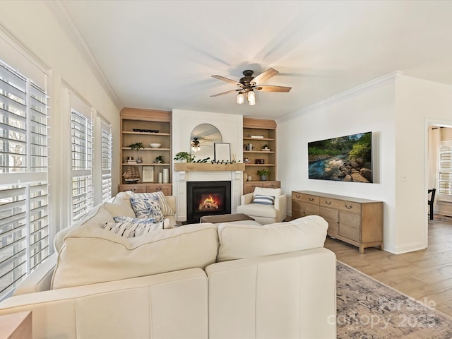 living room with ceiling fan, built in shelves, ornamental molding, and light hardwood / wood-style floors