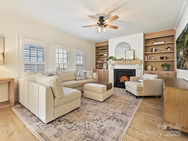 living room featuring ornamental molding, light hardwood / wood-style floors, ceiling fan, and a large fireplace