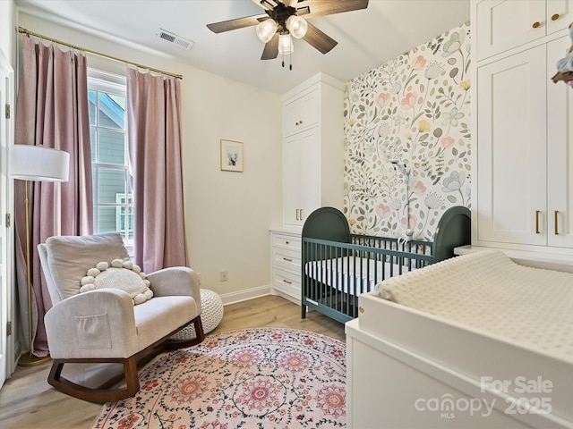 bedroom featuring light hardwood / wood-style floors, ceiling fan, and a nursery area