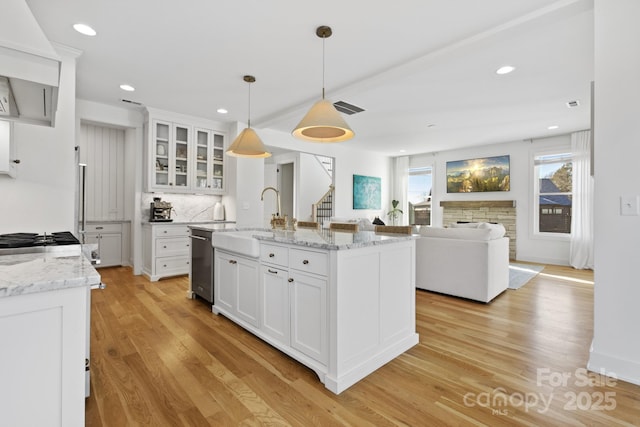 kitchen featuring decorative light fixtures, white cabinetry, sink, a center island with sink, and light wood-type flooring