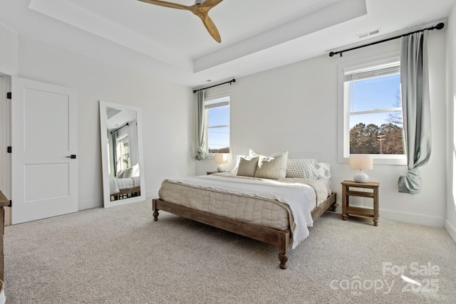 carpeted bedroom with multiple windows, ceiling fan, and a tray ceiling