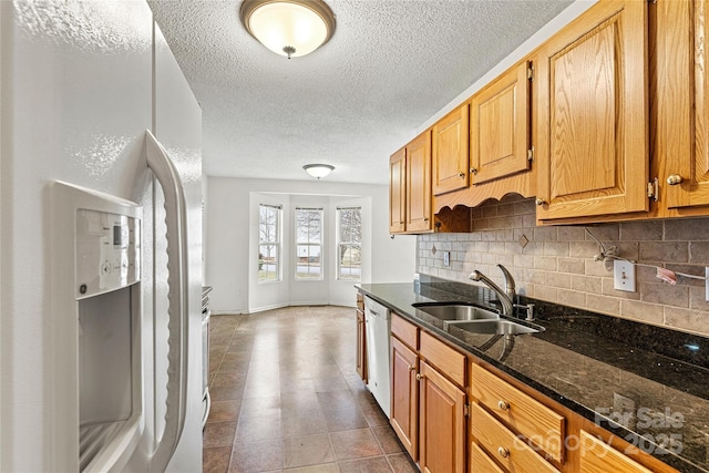 kitchen with white fridge with ice dispenser, stainless steel dishwasher, sink, backsplash, and dark stone counters