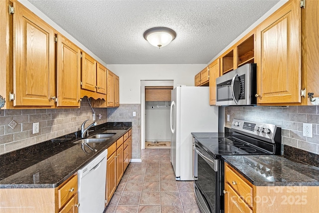 kitchen with appliances with stainless steel finishes, a textured ceiling, light tile patterned floors, sink, and dark stone countertops