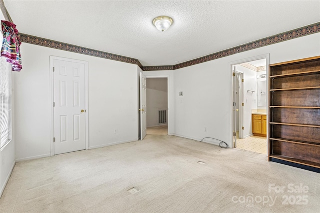 unfurnished bedroom with connected bathroom, light carpet, and a textured ceiling