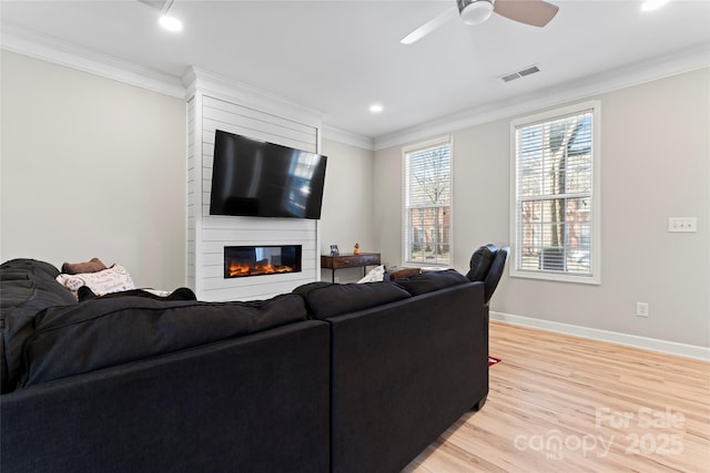 living room with a large fireplace, ceiling fan, light hardwood / wood-style flooring, and crown molding