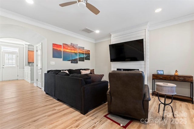 living room with ornamental molding, ceiling fan, and light wood-type flooring