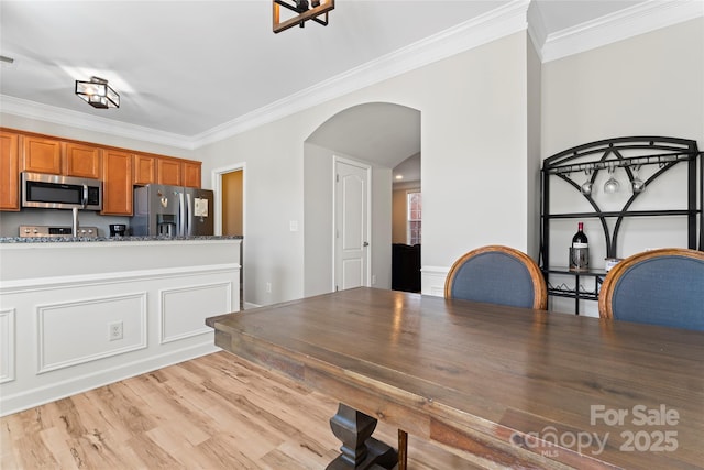 kitchen with light wood-type flooring, dark stone countertops, crown molding, and appliances with stainless steel finishes