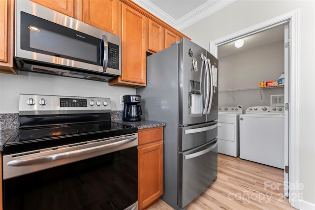 kitchen featuring dark stone counters, washer and clothes dryer, light hardwood / wood-style flooring, ornamental molding, and stainless steel appliances