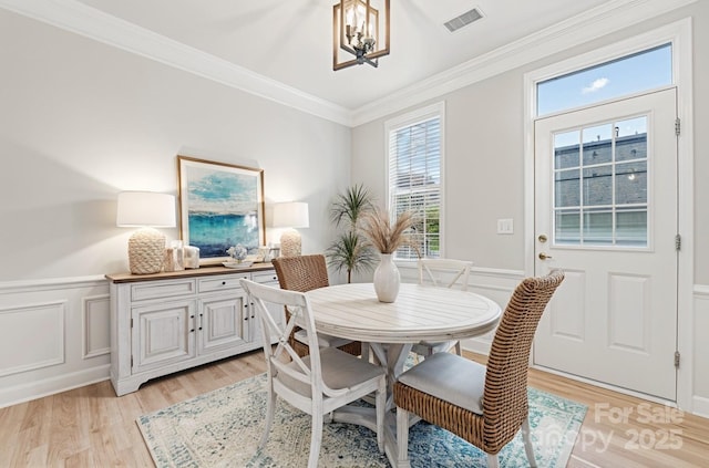 dining space with a chandelier, light wood-type flooring, ornamental molding, a decorative wall, and a wainscoted wall