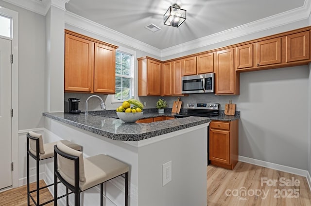 kitchen featuring stainless steel appliances, a breakfast bar area, brown cabinets, light wood-type flooring, and a peninsula