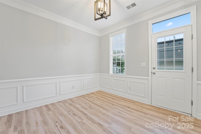entrance foyer with a chandelier, ornamental molding, light wood-style flooring, a wainscoted wall, and a decorative wall