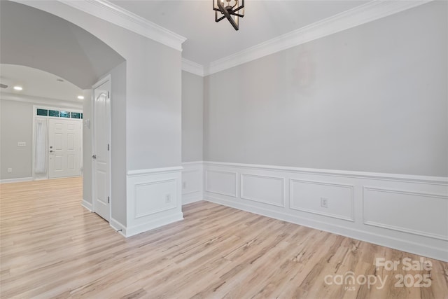 unfurnished room with arched walkways, light wood-style floors, ornamental molding, wainscoting, and a chandelier