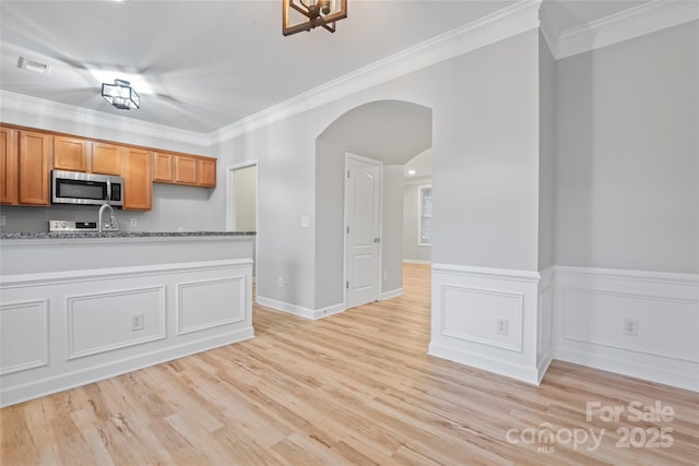 kitchen with stainless steel microwave, arched walkways, ornamental molding, light wood-type flooring, and brown cabinets