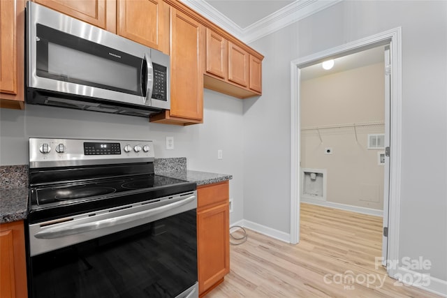 kitchen featuring appliances with stainless steel finishes, ornamental molding, light wood-type flooring, dark stone countertops, and baseboards