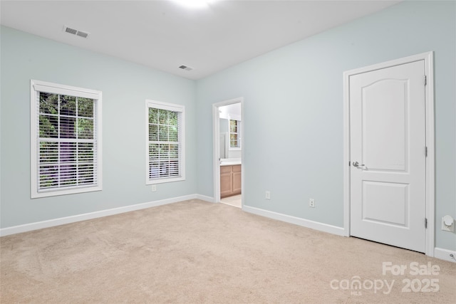 unfurnished bedroom with light colored carpet, baseboards, and connected bathroom