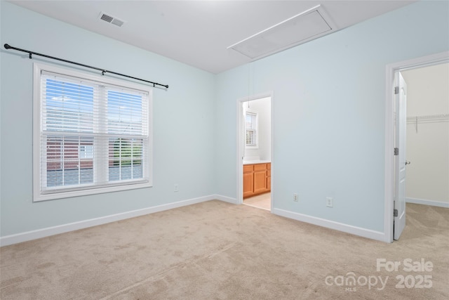 unfurnished bedroom featuring attic access, a spacious closet, light colored carpet, and baseboards