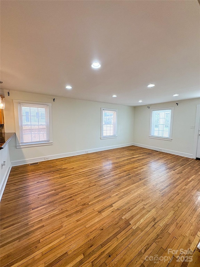 empty room featuring recessed lighting, plenty of natural light, wood finished floors, and baseboards