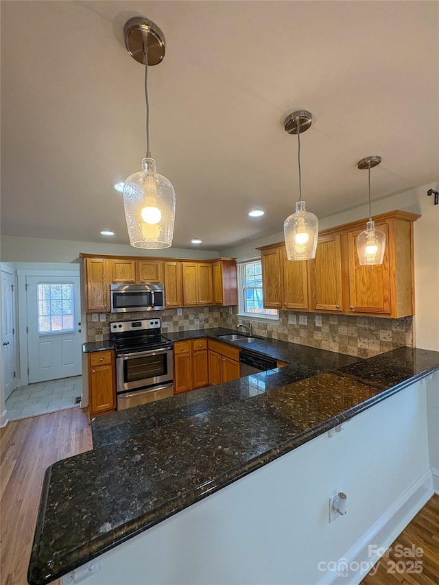 kitchen featuring light wood finished floors, decorative backsplash, brown cabinets, stainless steel appliances, and a sink