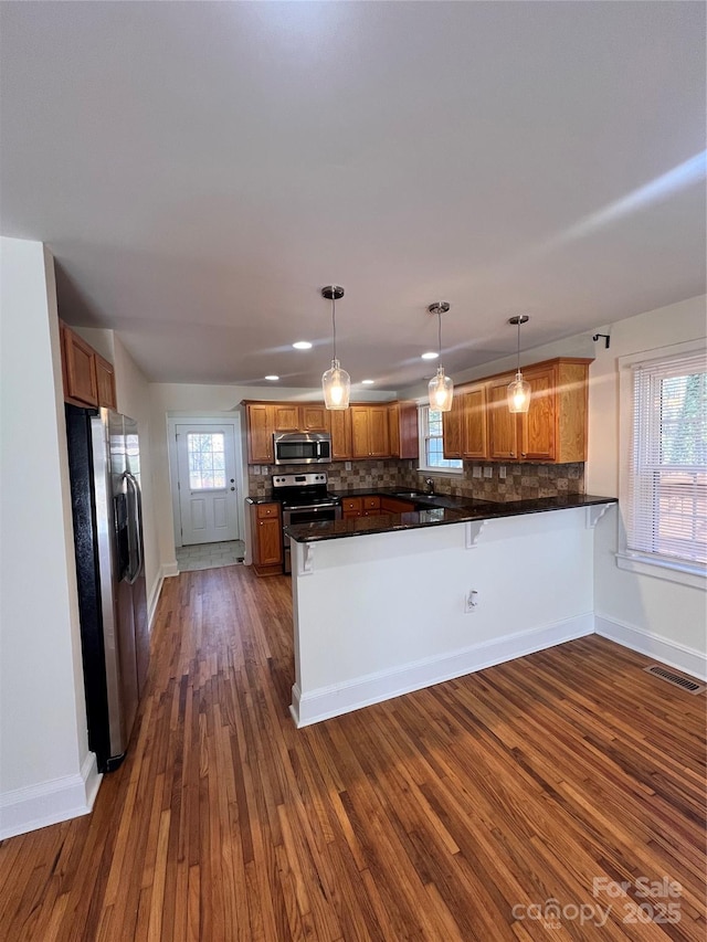 kitchen featuring visible vents, brown cabinetry, a peninsula, stainless steel appliances, and backsplash