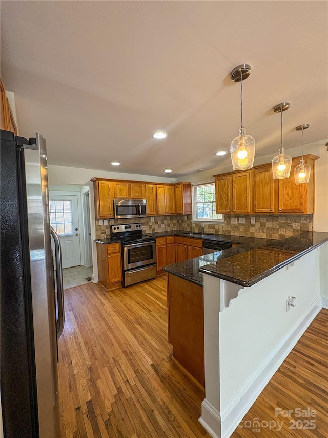 kitchen with a peninsula, light wood-style floors, brown cabinets, and stainless steel appliances