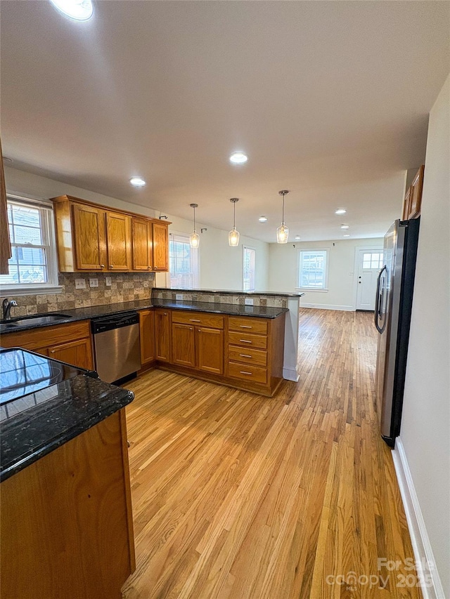 kitchen featuring brown cabinets, light wood finished floors, appliances with stainless steel finishes, a sink, and a peninsula