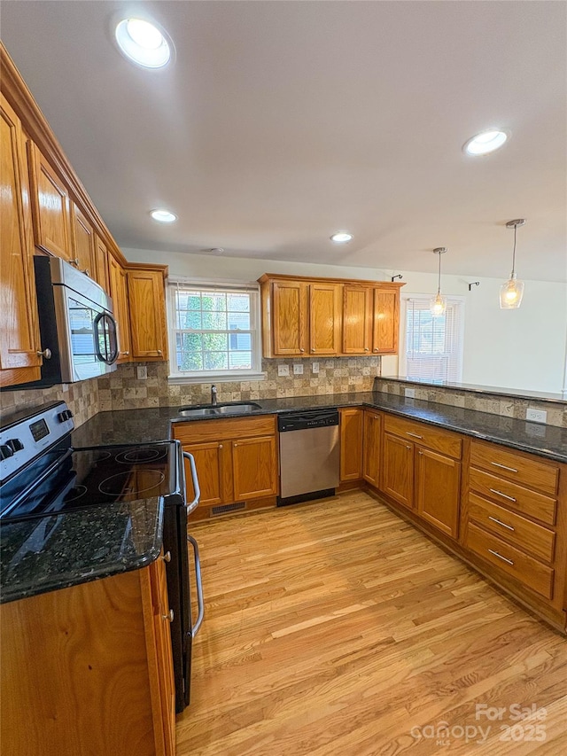 kitchen featuring stainless steel appliances, a sink, decorative backsplash, light wood finished floors, and brown cabinetry