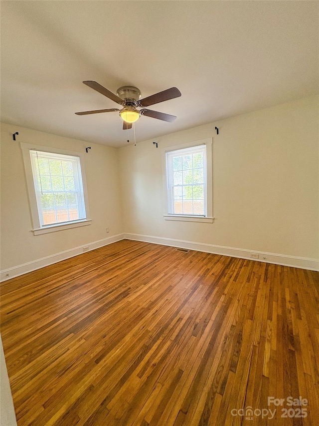 spare room featuring ceiling fan, visible vents, baseboards, and hardwood / wood-style floors