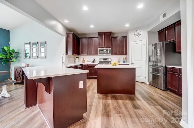 kitchen with stainless steel appliances, a peninsula, visible vents, and light wood-style floors