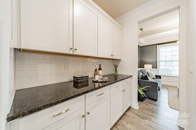 kitchen with white cabinets, dark stone counters, tasteful backsplash, light hardwood / wood-style flooring, and crown molding