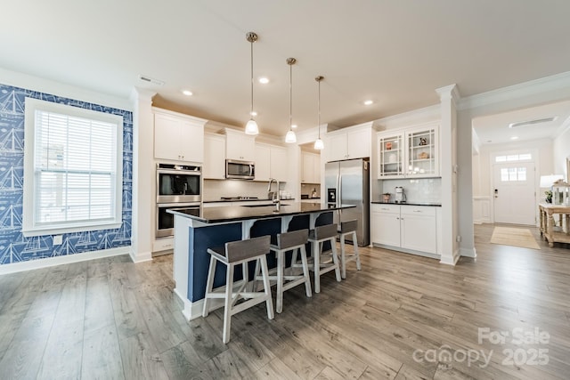 kitchen featuring hanging light fixtures, white cabinetry, a center island with sink, light hardwood / wood-style floors, and stainless steel appliances