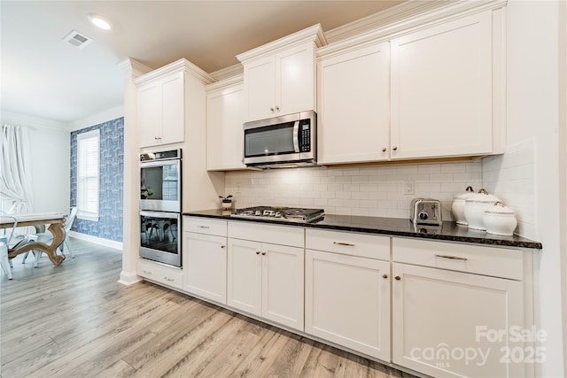 kitchen featuring white cabinets, stainless steel appliances, dark stone counters, decorative backsplash, and light wood-type flooring