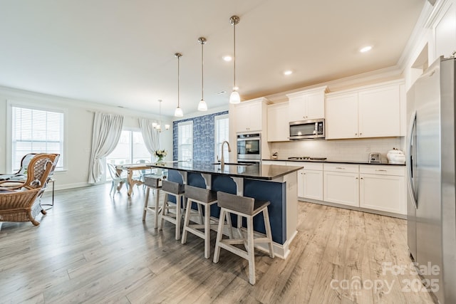 kitchen featuring crown molding, pendant lighting, appliances with stainless steel finishes, white cabinets, and an island with sink