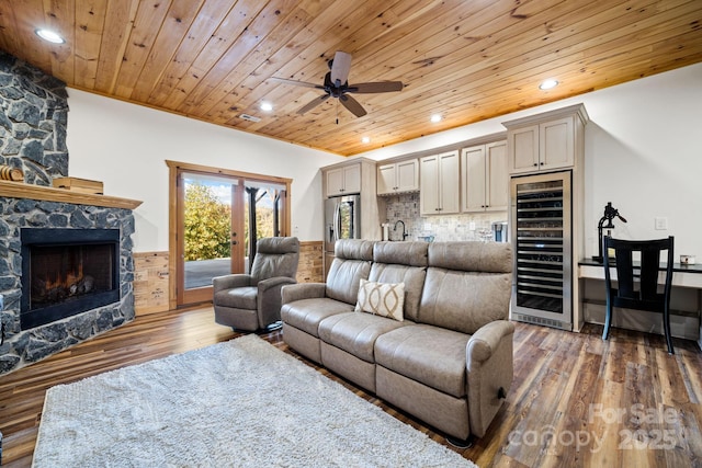 living room with dark hardwood / wood-style floors, wood ceiling, a stone fireplace, and beverage cooler