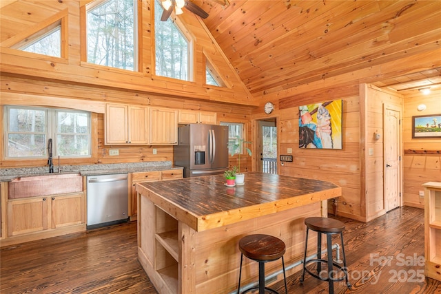 kitchen with a kitchen island, appliances with stainless steel finishes, light brown cabinets, and wood walls