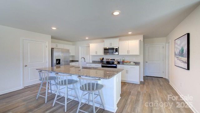 kitchen with white cabinets, appliances with stainless steel finishes, sink, a kitchen island with sink, and light hardwood / wood-style flooring